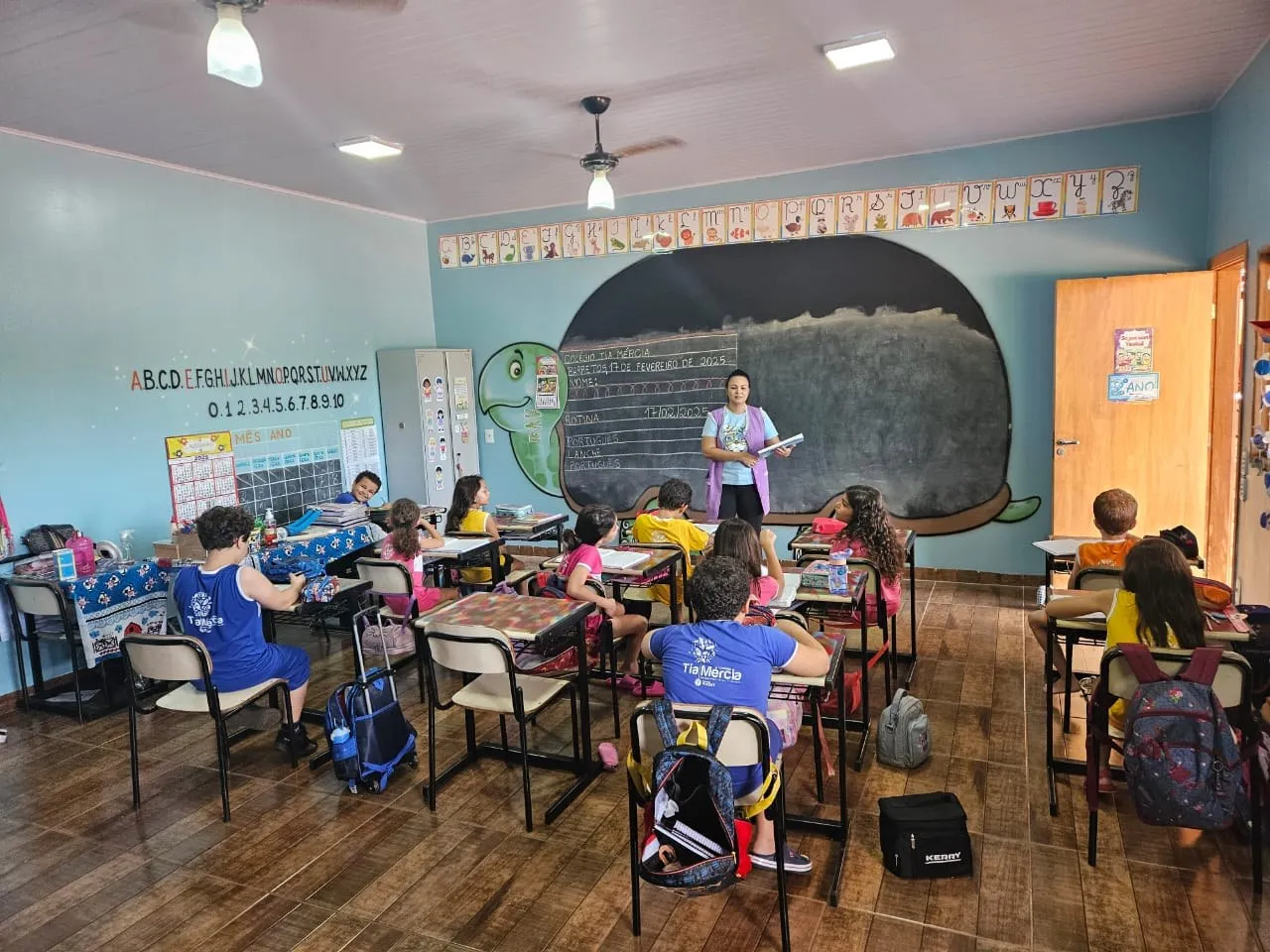 Professora diante da lousa em formato de tartaruga, com a turma em suas carteiras
