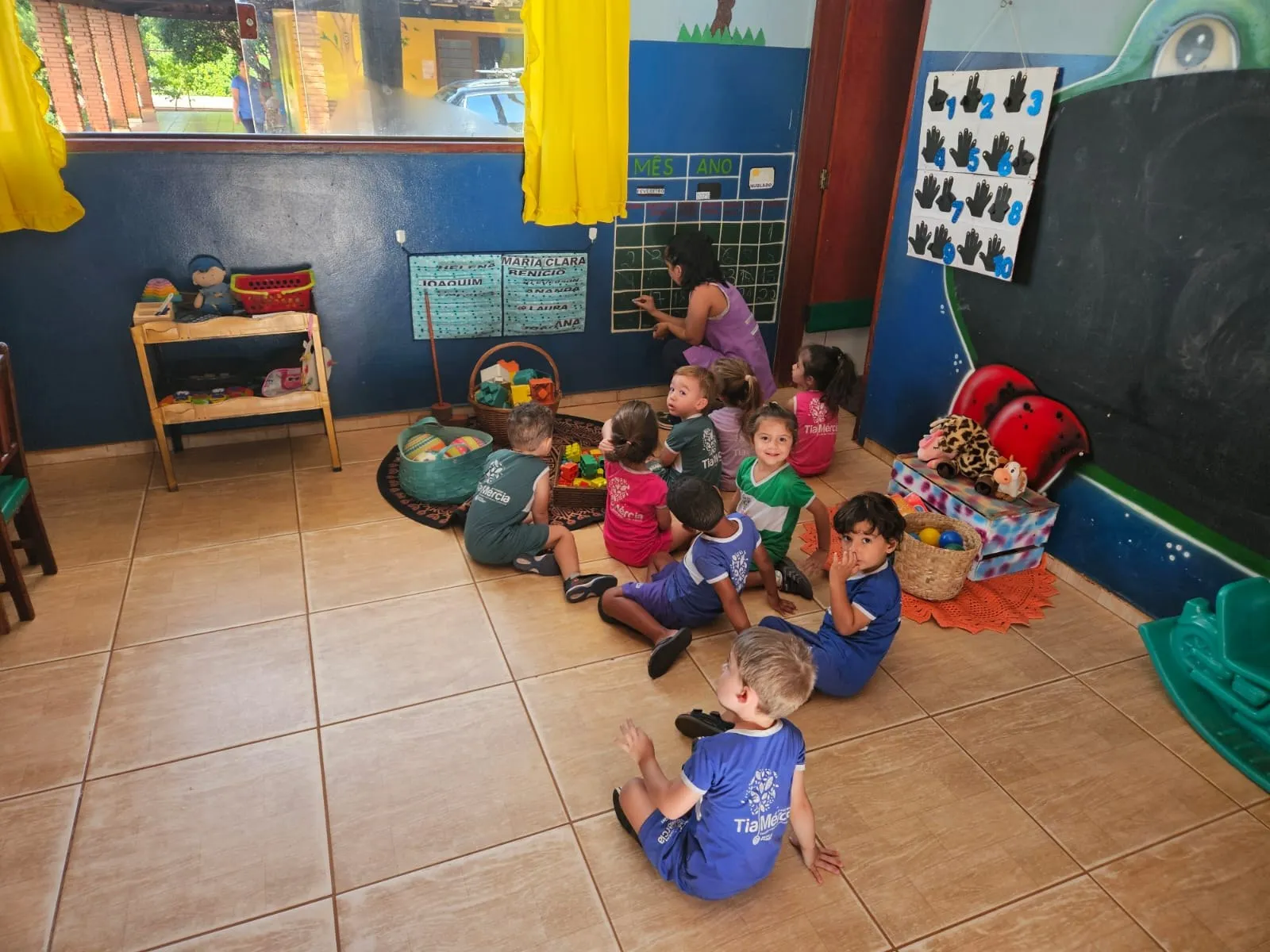 Crianças sentadas no chão em roda, com cestos de brinquedos