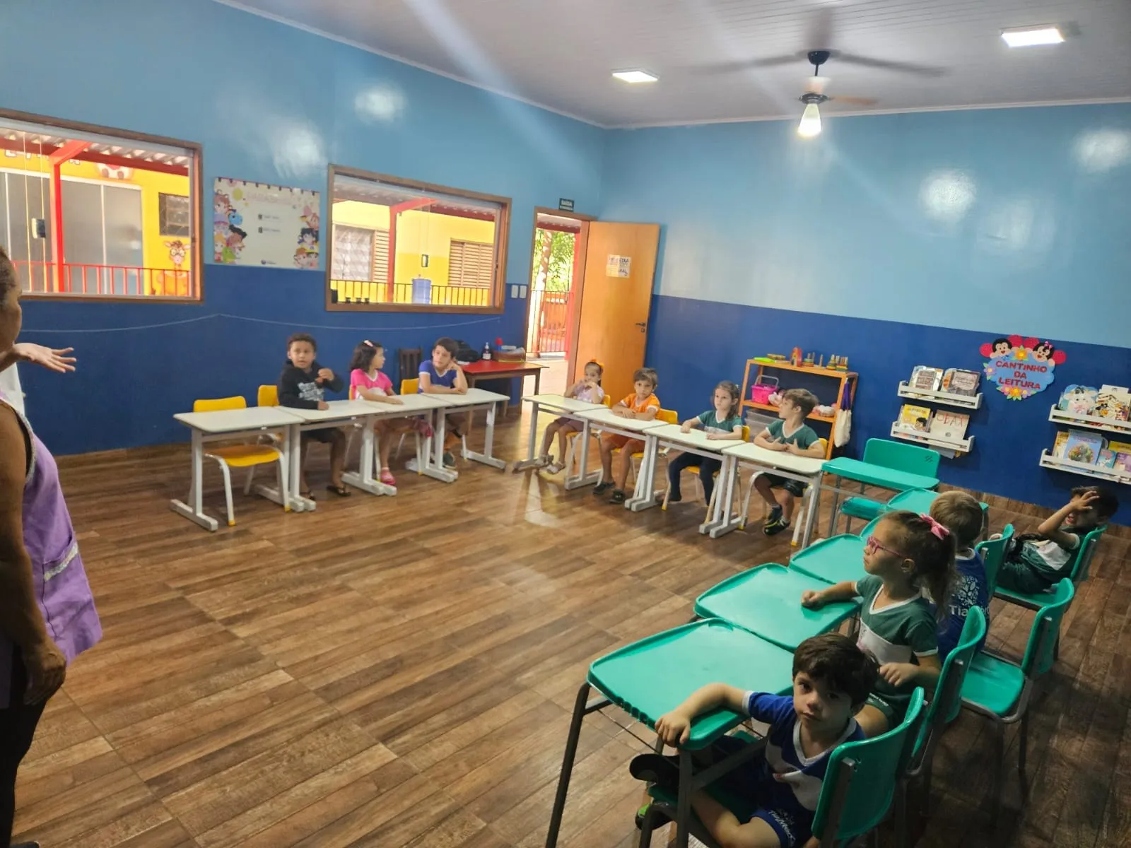 Sala ampla com carteiras verde-água e alunos sentados
