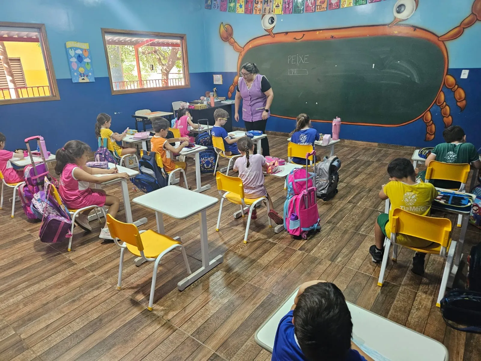 Professora ajudando os alunos, em sala com lousa em formato de caranguejo