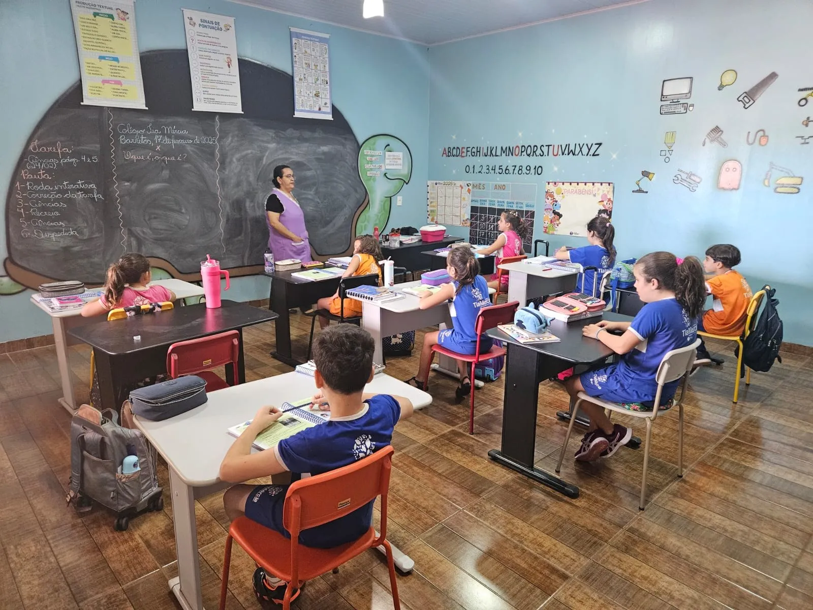 Professora junto à lousa, com alunos do Fundamental em suas carteiras