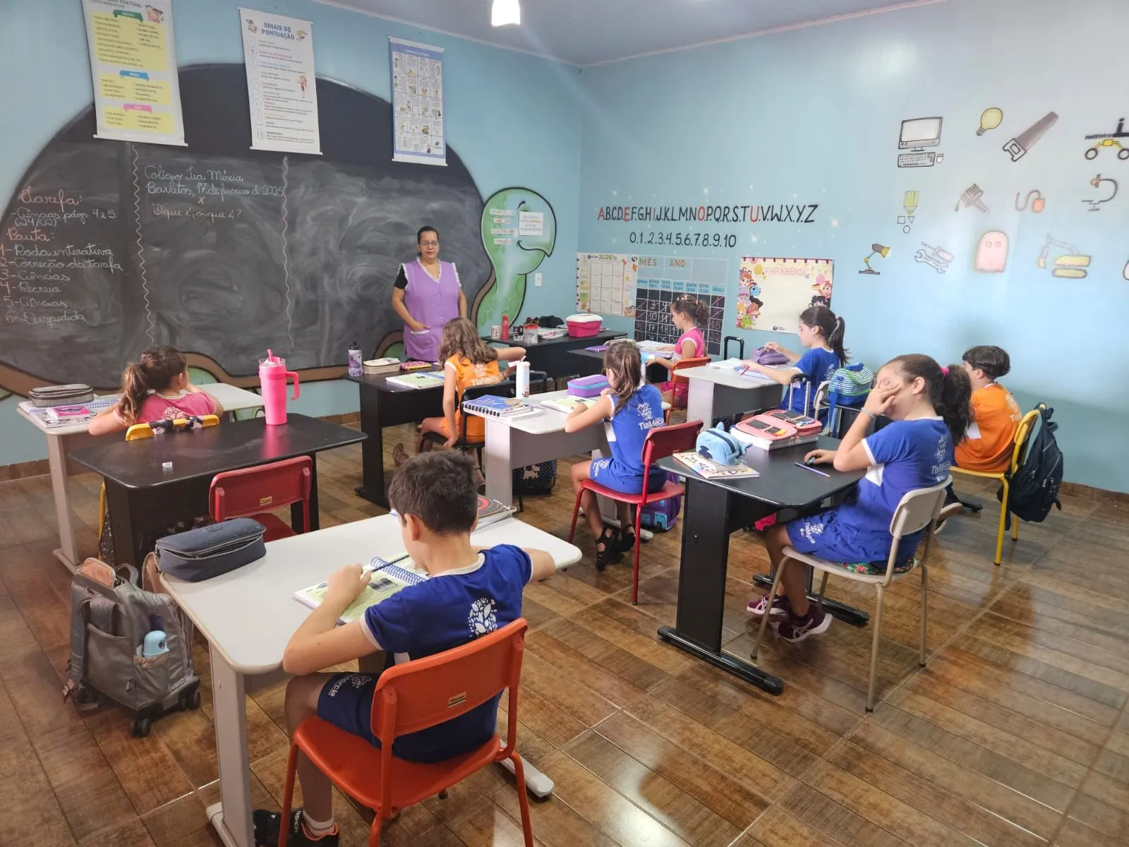 Alunos do Fundamental estudando em suas carteiras, com alfabeto e numerais na parede